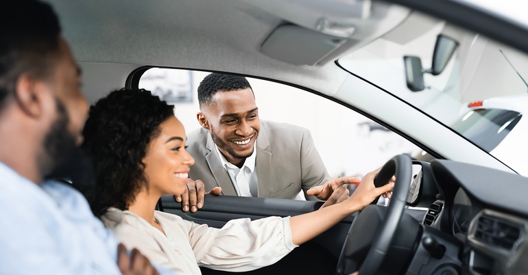 Couple testing out sitting in a new car with car salesman smiling looking on