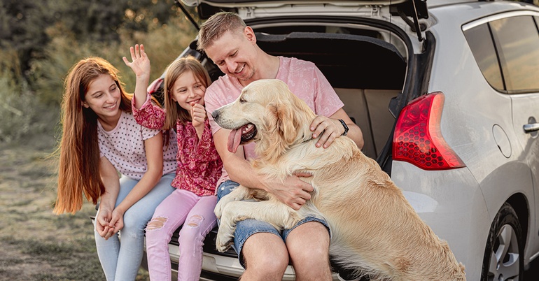 Family with dog sitting in open truck of their car in a nature setting